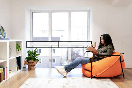 Smiling black woman reading book and drinking coffee