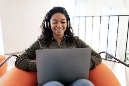 Smiling black woman in headset using pc at home
