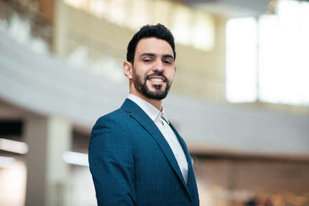Smiling confident attractive young arab guy, general manager with beard in suit looks at cameraの写真素材