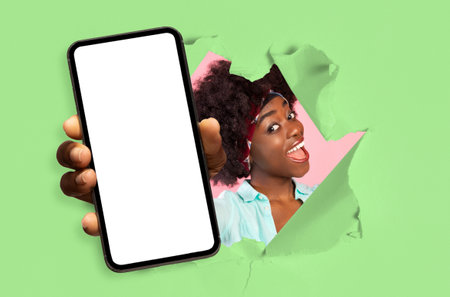 Happy excited young african american female with open mouth looks through hole in green paper and...