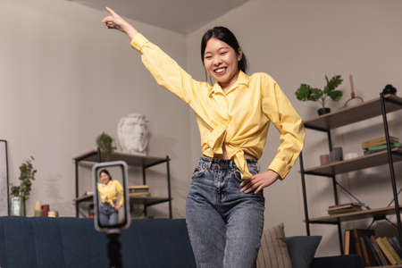 Cheerful Asian woman dancing at camera filming video on cellphoneの写真素材