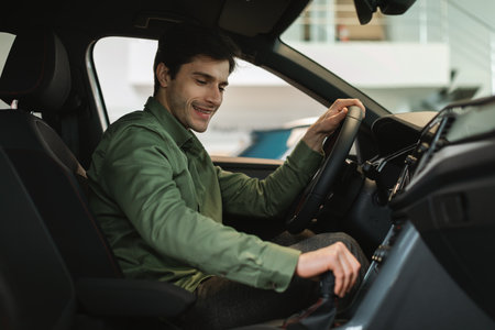 Happy young Caucasian man test driving new car before purchase at modern automobile dealership, copy...