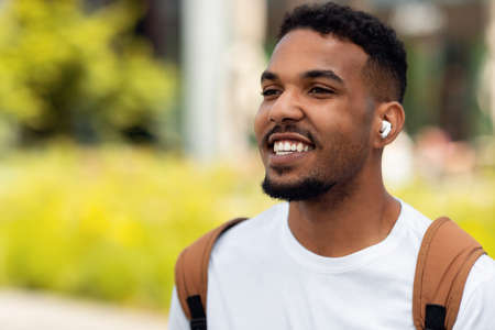 Happy young man listening to music in earbuds walking outdoorsの写真素材
