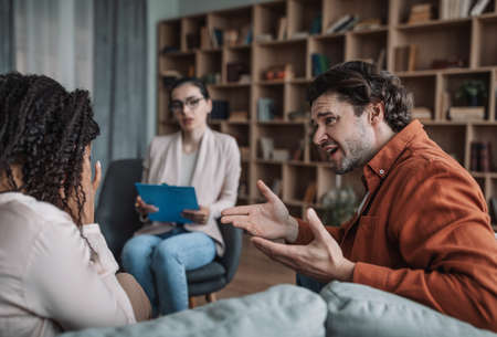 Serious young caucasian woman psychologist consults international couple in modern clinic interiorの写真素材