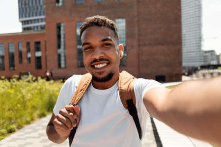 Happy young man taking selfie picture in earbuds walking outdoors