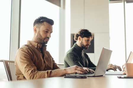 Focused company employees using laptop computers, working together at modern office, copy space....