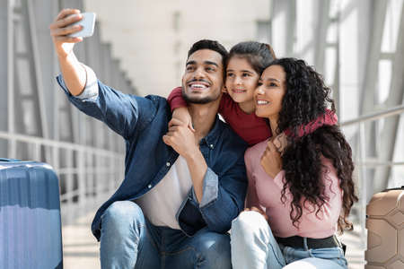 Joyful Middle Eastern Family Of Three Taking Selfie With Smartphone In Airportの写真素材