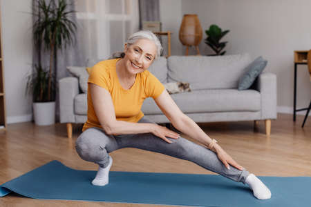 Active senior woman doing stretching exercises during her home workout, training, keeping fit and healthyの写真素材