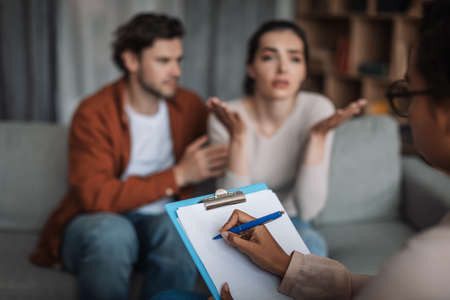 Depressed sad young european husband calm, support wife talking to psychologist in clinic interior