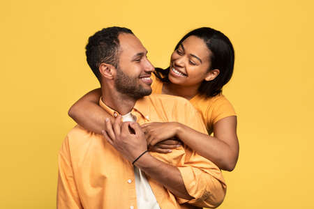 Affectionate young black woman hugging her boyfriend, looking in his eyes on yellow studio backgroundの写真素材