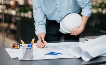 Cropped millennial middle eastern engineer with hard hat works with drawings at workplace in officeの写真素材