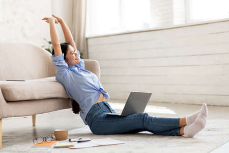 Joyful chinese woman stretching while using laptop