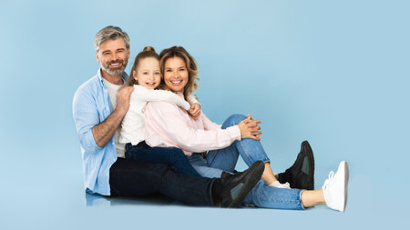 Middle Aged Parents And Daughter Hugging Sitting Over Blue Background
