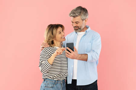 Happy Couple Using Smartphone, Wife Pointing At Phone, Pink Backgroundの写真素材