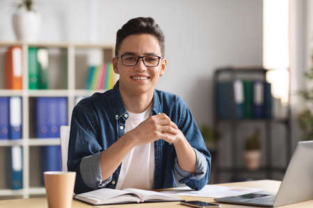 Portrait Of Young Male Entrepreneur Posing At Desk With Laptop In Office