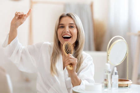 Joyful pretty adult lady singing while brushing her hairの写真素材