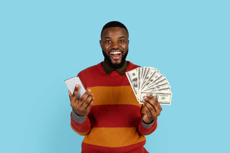 Online Profit. Joyful black male holding smartphone and dollar cash