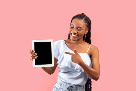 Charming young black woman showing tablet with empty screen on pink background, mockup for website...