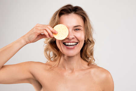 Skincare Fun. Middle Aged Woman Covering Eye With Cosmetic Sponge And Laughingの写真素材