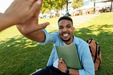 Happy african american guy giving high five, celebrating academic success and passed exam, sitting...