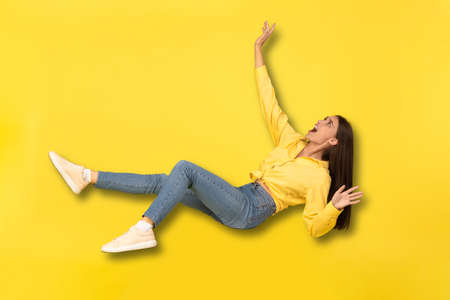 Scared Millennial Lady Falling In Mid-Air Shouting Over Yellow Backgroundの写真素材