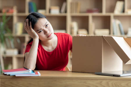 Unhappy sad disappointed teen girl sitting with cardboard box in living room interiorの写真素材