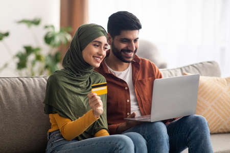 Middle Eastern Spouses Shopping Online Via Laptop Holding Card Indoorの写真素材