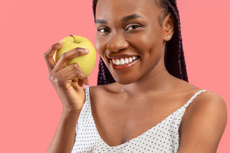 Healthy diet and lifestyle. Happy young black lady holding fresh green apple and smiling, recommending eating fruitsの写真素材