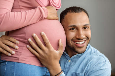 Happy black man embracing belly of his pregnant muslim wife in hijab