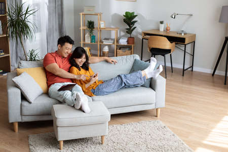 Relaxed japanese couple chilling together at home, using gadgetsの写真素材