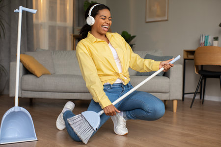 Black Lady Sweeping Floor Having Fun Pretending Playing Guitar Indoorの写真素材