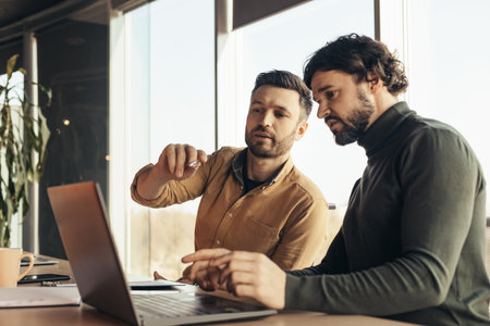 Experienced mentor explaining to young colleague business project strategy at office interior, blank spaceの写真素材