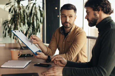 Partnership concept. Two serious businessmen studying documents, discussing business deal in office...