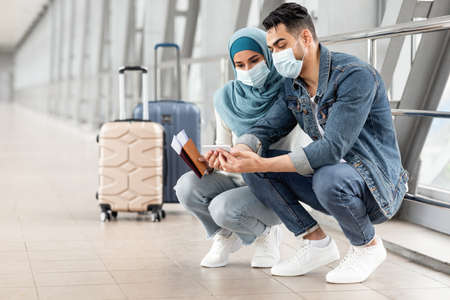 Islamic Couple Wearing Masks Using Smartphone While Waiting For Flight In Airportの写真素材