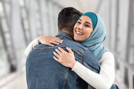 Happy Reunion. Joyful Muslim Woman In Hijab Hugging Her Husband At Airportの写真素材