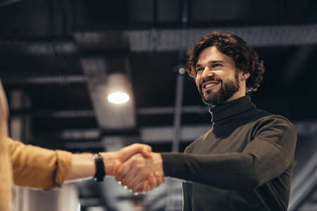 Business partnership. Smiling entrepreneur handshaking with partner after successful negotiations at modern officeの写真素材