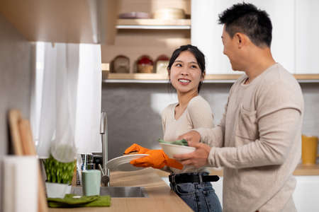 Happy asian couple washing dishes together at homeの写真素材