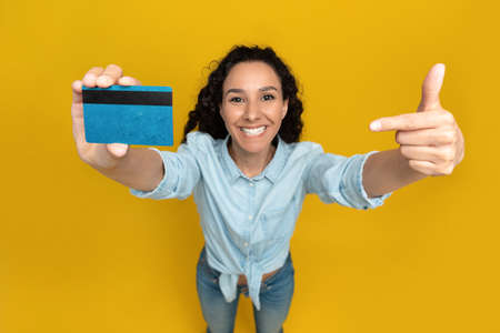 Above view of attractive young woman pointing at credit card over yellow studio background. Financial services conceptの写真素材