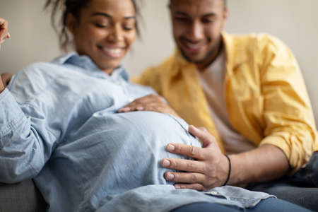 Black Spouses Expecting Baby, Husband Touching Pregnant Wifes Belly Indoorの写真素材