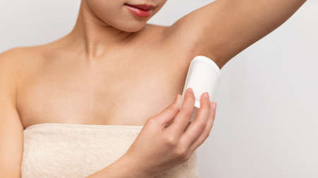 Closeup of young lady applying deodorant antiperspirant on armpit, standing over white studio backgroundの写真素材