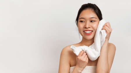 Happy beautiful asian lady drying face with soft towel looking aside, posing over white studio background, free spaceの写真素材