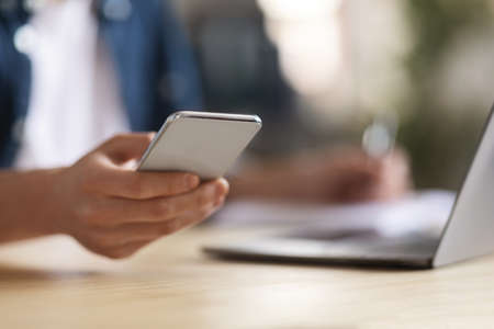 Young Male Using Modern Smartphone While Sitting At Desk With Laptop