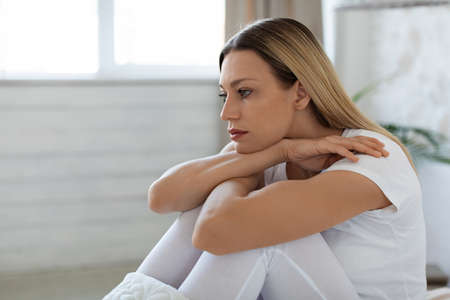 Depressed young woman sitting on bed alone at home