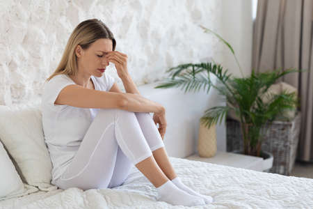 Young woman in pain sitting on bed, toching her headの写真素材