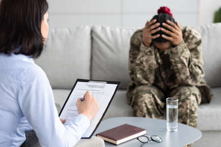 Psychotherapist Lady Making Psychology Survey With Depressed Black Female Soldier In Uniformの写真素材
