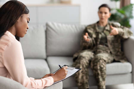 Black Female Psychotherapist Taking Notes During Therapy Session With Military Womanの写真素材