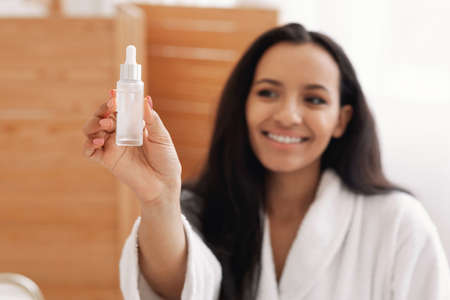 Black Lady Showing Cosmetic Bottle Advertising Facial Serum In Bathroomの写真素材