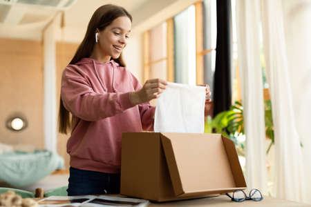 Young satisfied buyer. Happy teen girl received package, unpacking cardboard box, looking insideの写真素材