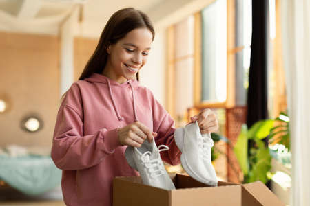 Happy teen girl buyer holding new footwear unpacking cardboard box, receiving shoes after successful online shoppingの写真素材