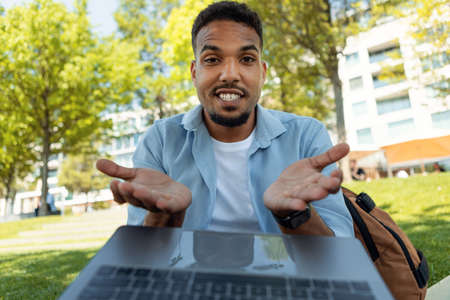 Excited young black guy talking to family or friend on laptop, gesturing at webcamera, sitting...